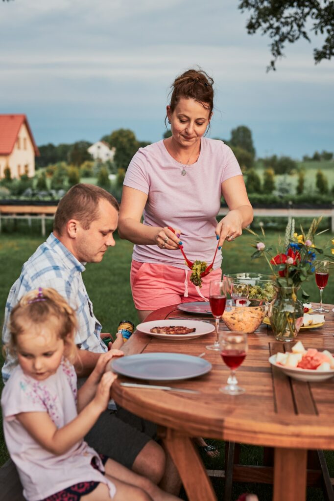 Family having a meal from grill during summer picnic outdoor dinner in a home garden.