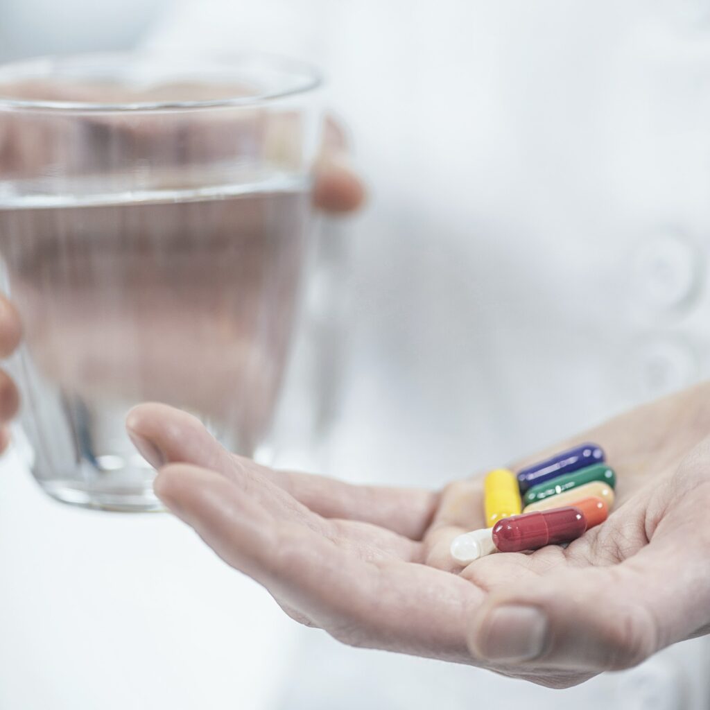 Hands with Colorful Pills and a Glass of Water