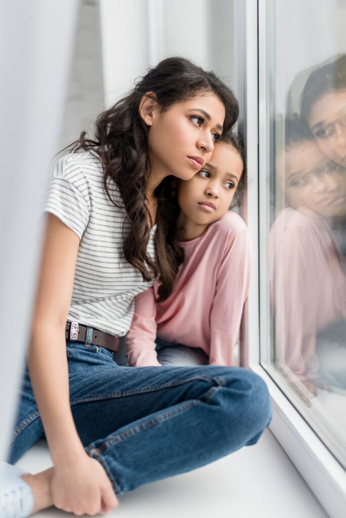 sad mother and daughter looking through window
